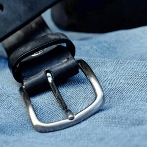 Close-up of a black leather belt with metal buckle laid on blue denim fabric.