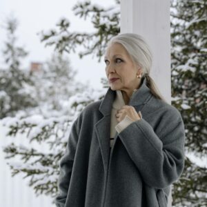 Sophisticated senior woman in a gray coat enjoying a serene winter setting outdoors.